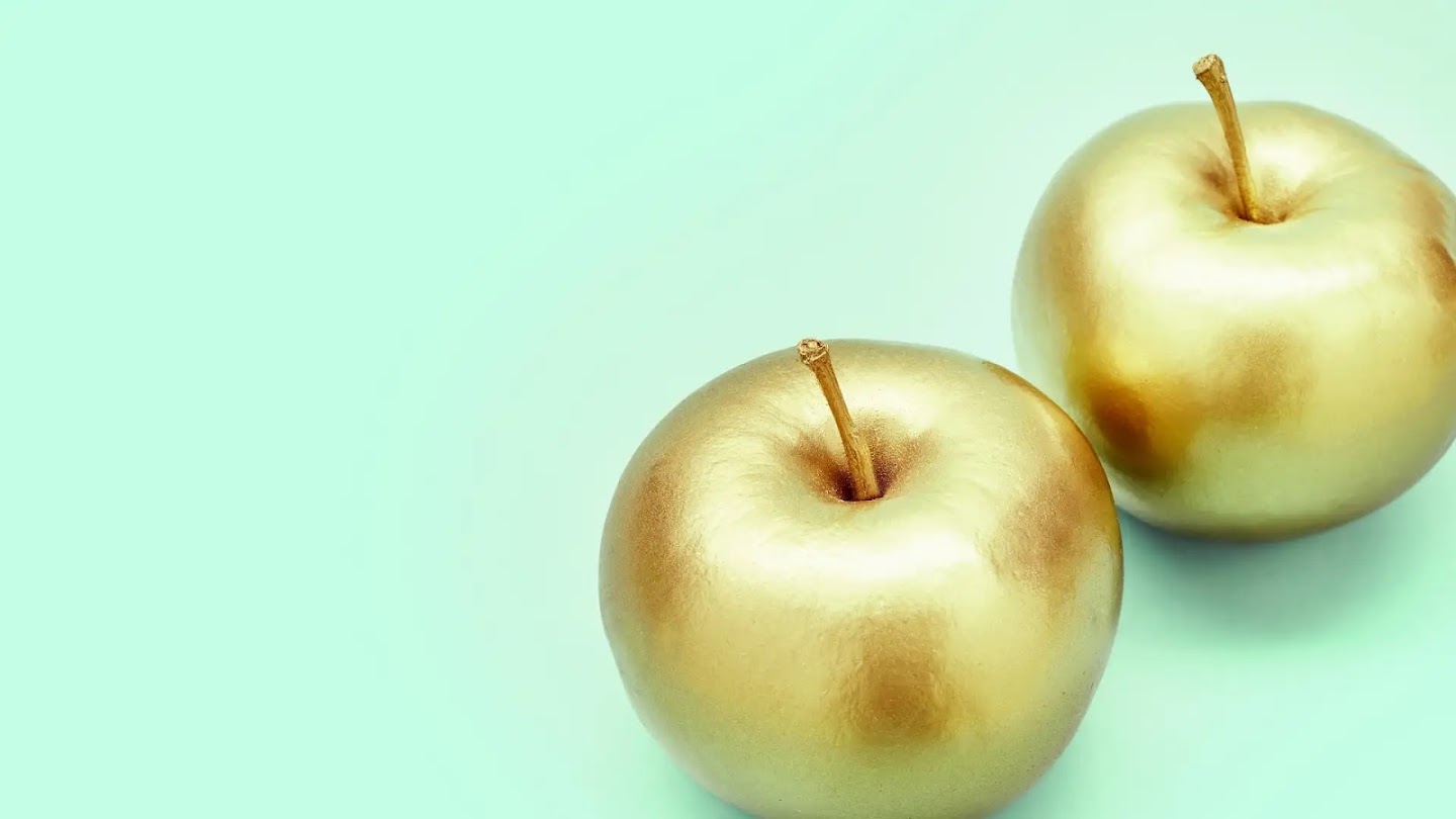 Two golden apples sitting on a pale green surface.