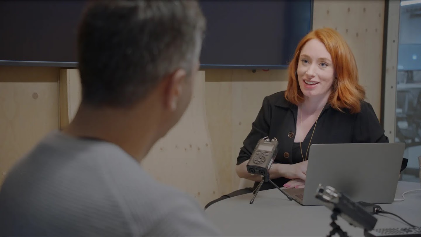 Mathematician and broadcaster Dr Hannah Fry sits in a recording booth speaking to a man with his back to the camera.