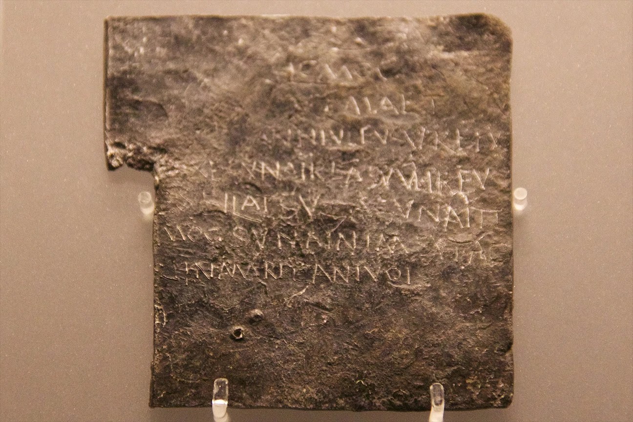 An ancient Roman lead curse tablet (Tabella Sulis 97) from Aquae Sulis, showing scratched Latin inscriptions on a weathered metal sheet.