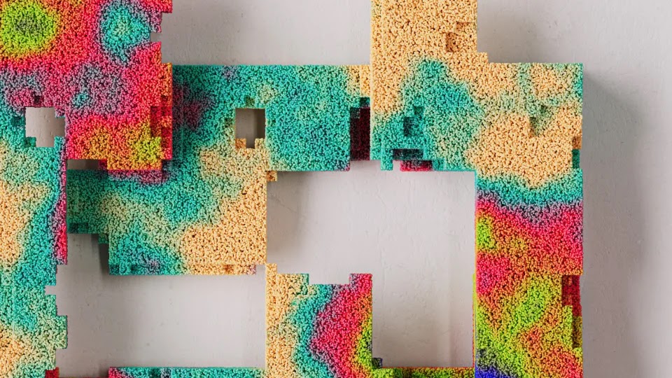 A tactile art piece made of a dense collection of tiny, multi-colored spheres creating a topographic heat map effect in vibrant shades of pink, orange, green, and teal, with several square sections cut out of the surface.
