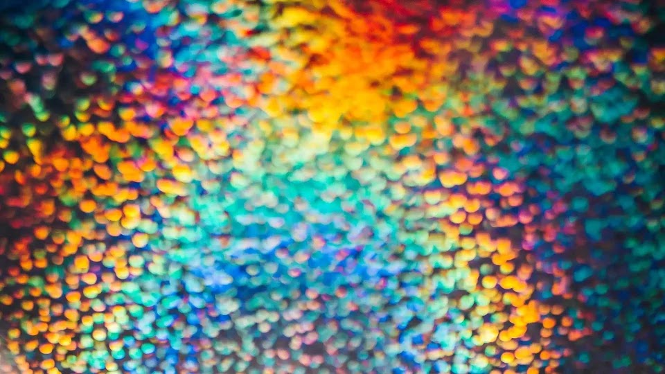 A close-up, out-of-focus background of multi-colored light orbs, creating a soft, bokeh effect with a palette ranging from deep blues and purples to bright oranges and yellows.
