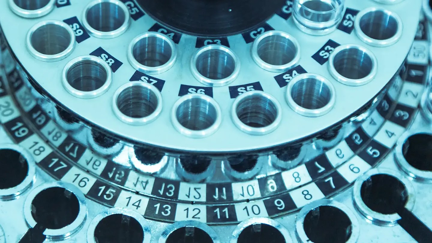 A close-up of a metallic laboratory sample carousel with numbered slots.